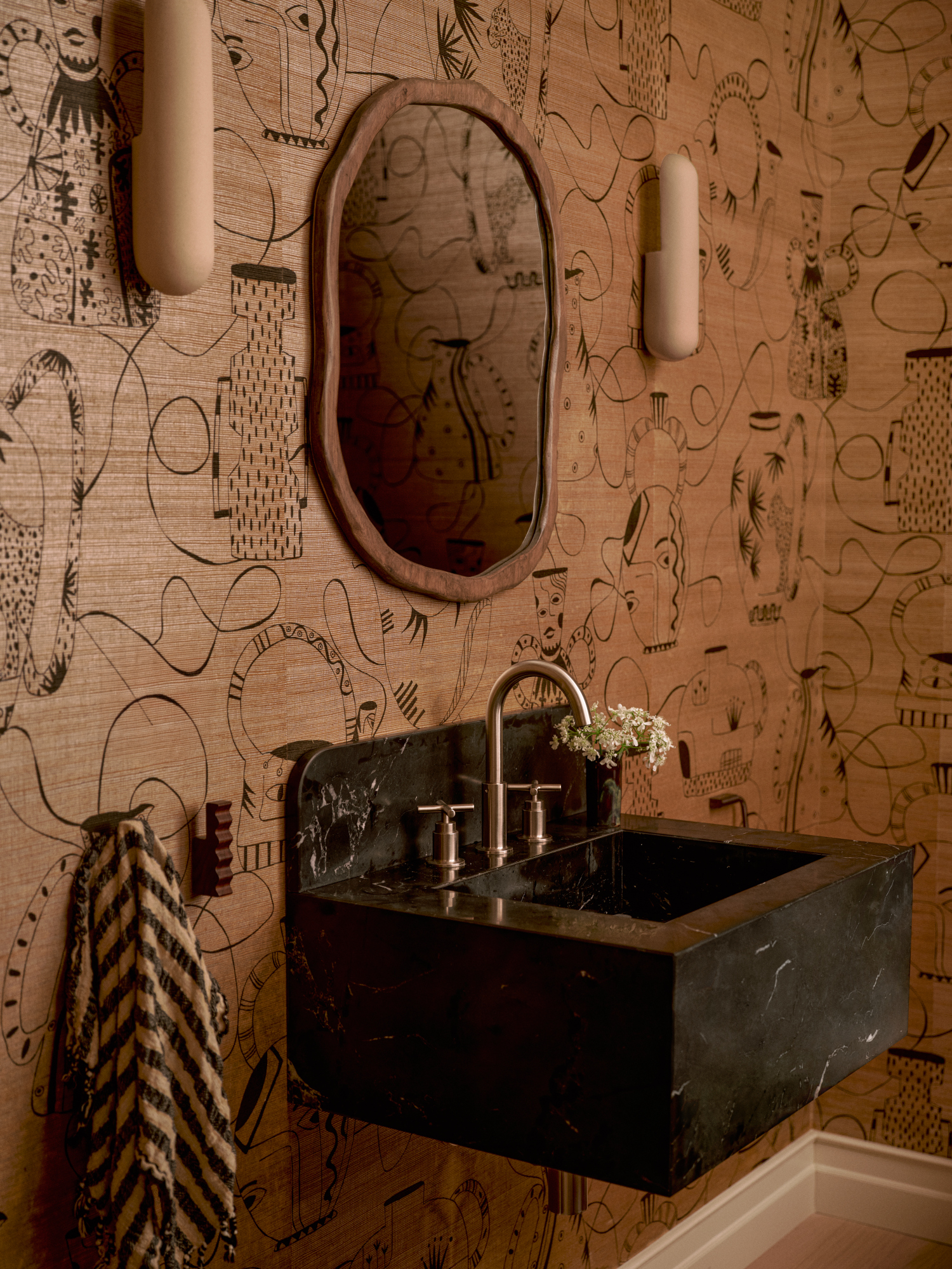 Powder room with beige line-drawn patterned wallpaper, black stone sink, organic wood mirror and beige pill-shaped wall lights