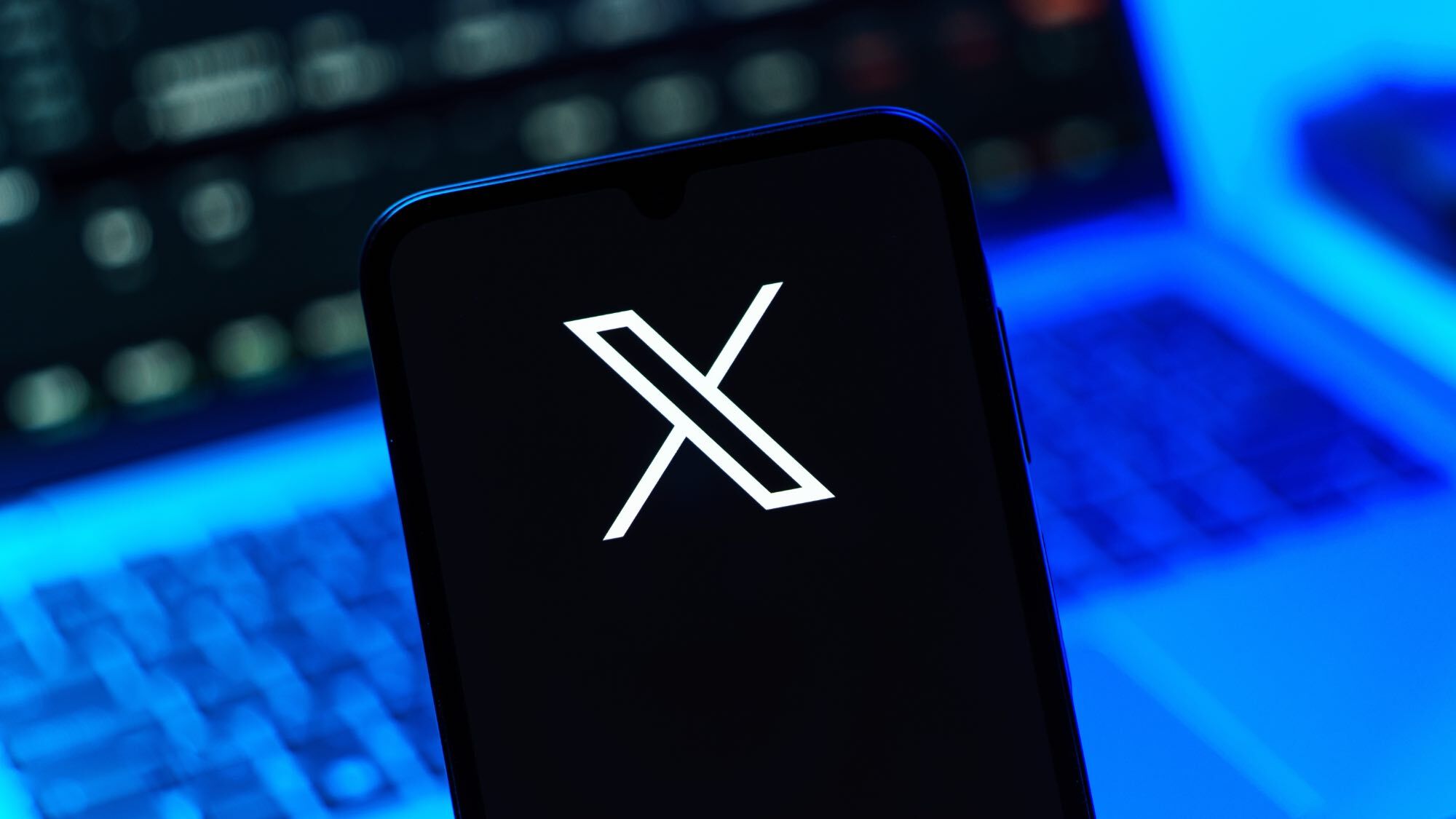 The X icon on a smartphone in front of a laptop