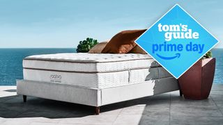 The Saatva Classic Mattress on a bed foundation outdoors, overlooking the sea. A Tom's Guide Prime Day deals graphic in the top left corner