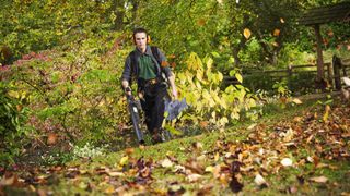 Man using a leaf blower outside in an autumn field environment.