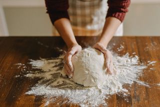 A person kneading dough on a wooden kitchen surface.