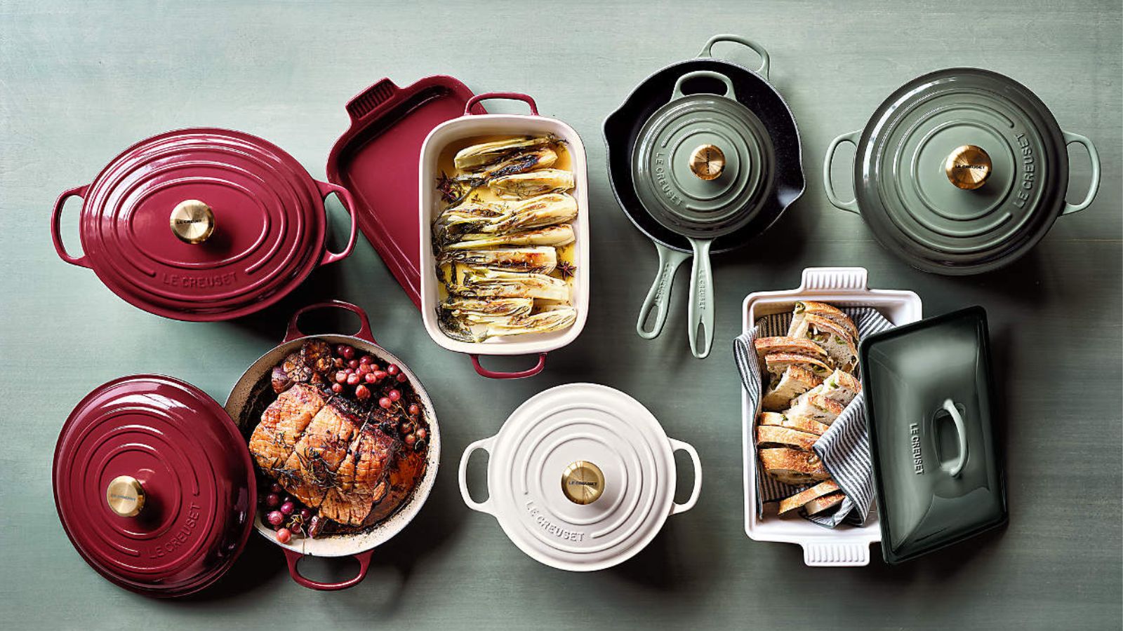 Red, white and pale green Le Creuset cookware on a pale green wooden background