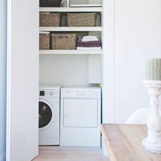 White utility cupboard with washing machine and tumble dryer, and shelves above them