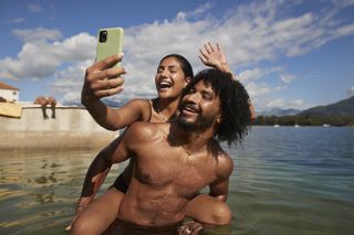 Couple in the sea on holiday - woman is on the man's back and taking a photo of the couple using a smart phone