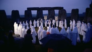 A large crowd of druids dressed in white robes at a nighttime gathering at Stonehenge in Wiltshire, England.