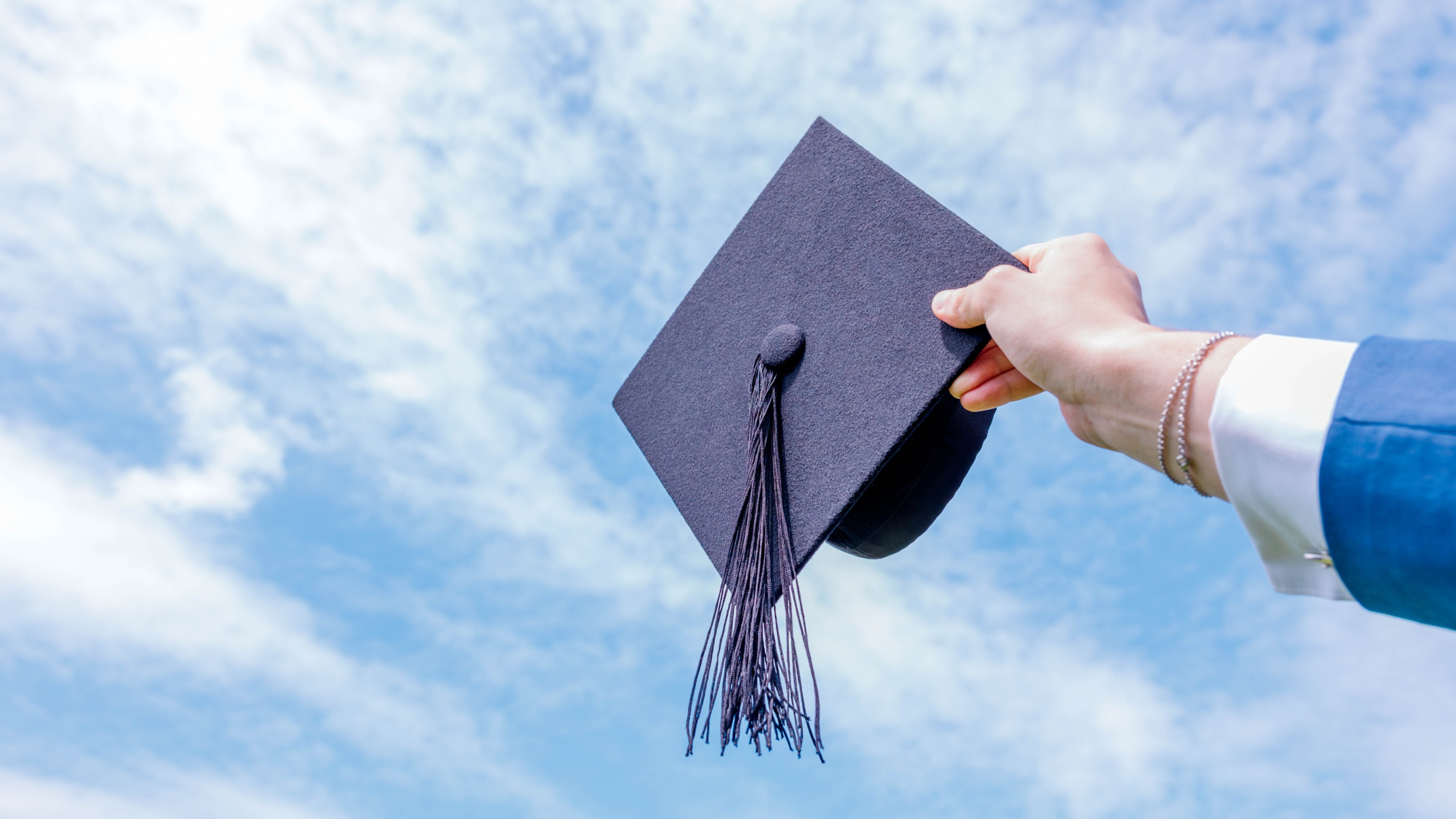 A close-up shot of a student&#039;s hand throwing a hat into the sky during a graduation celebration