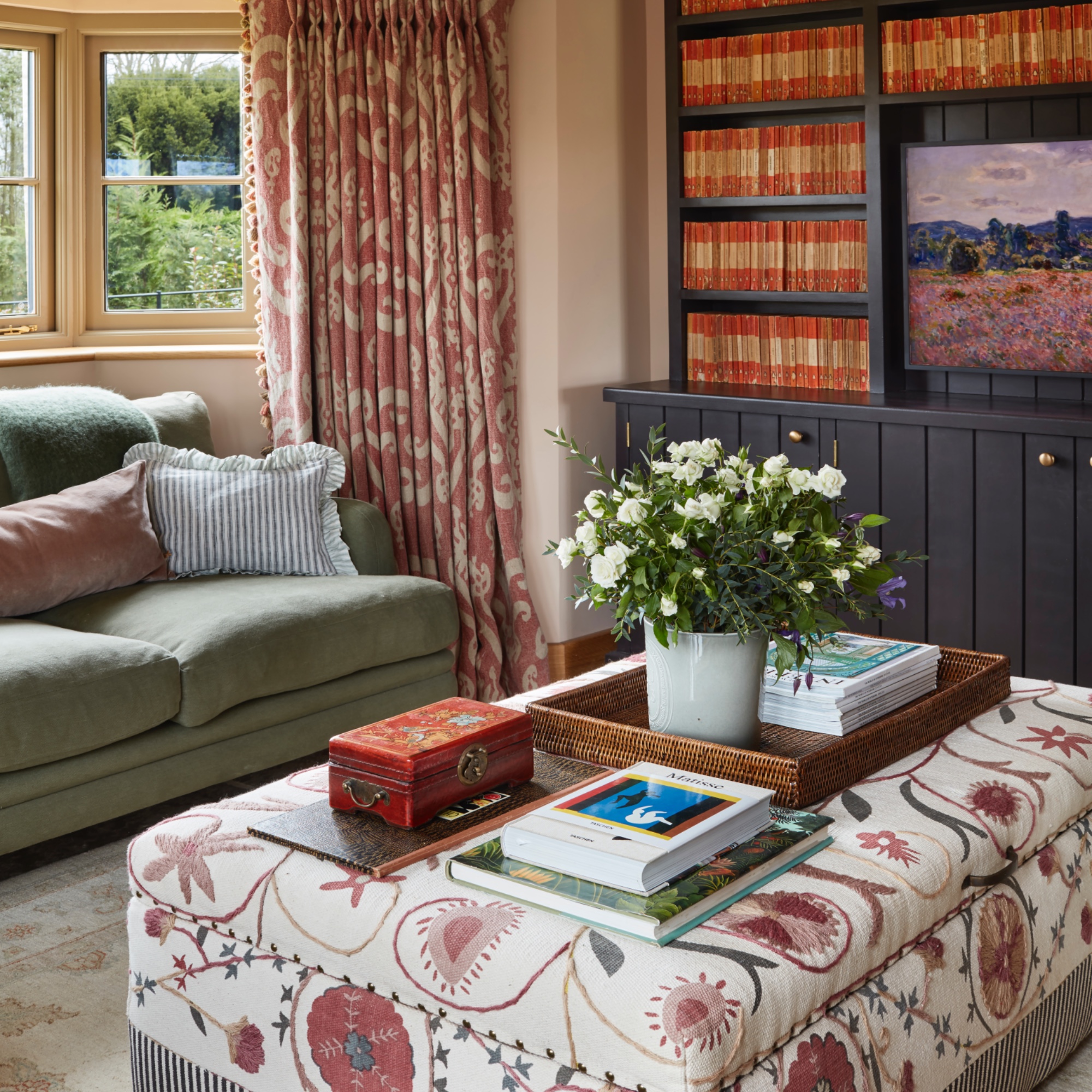 cosy living room with patterned upholstered footstool, bookcase, green sofa, patterned curtains