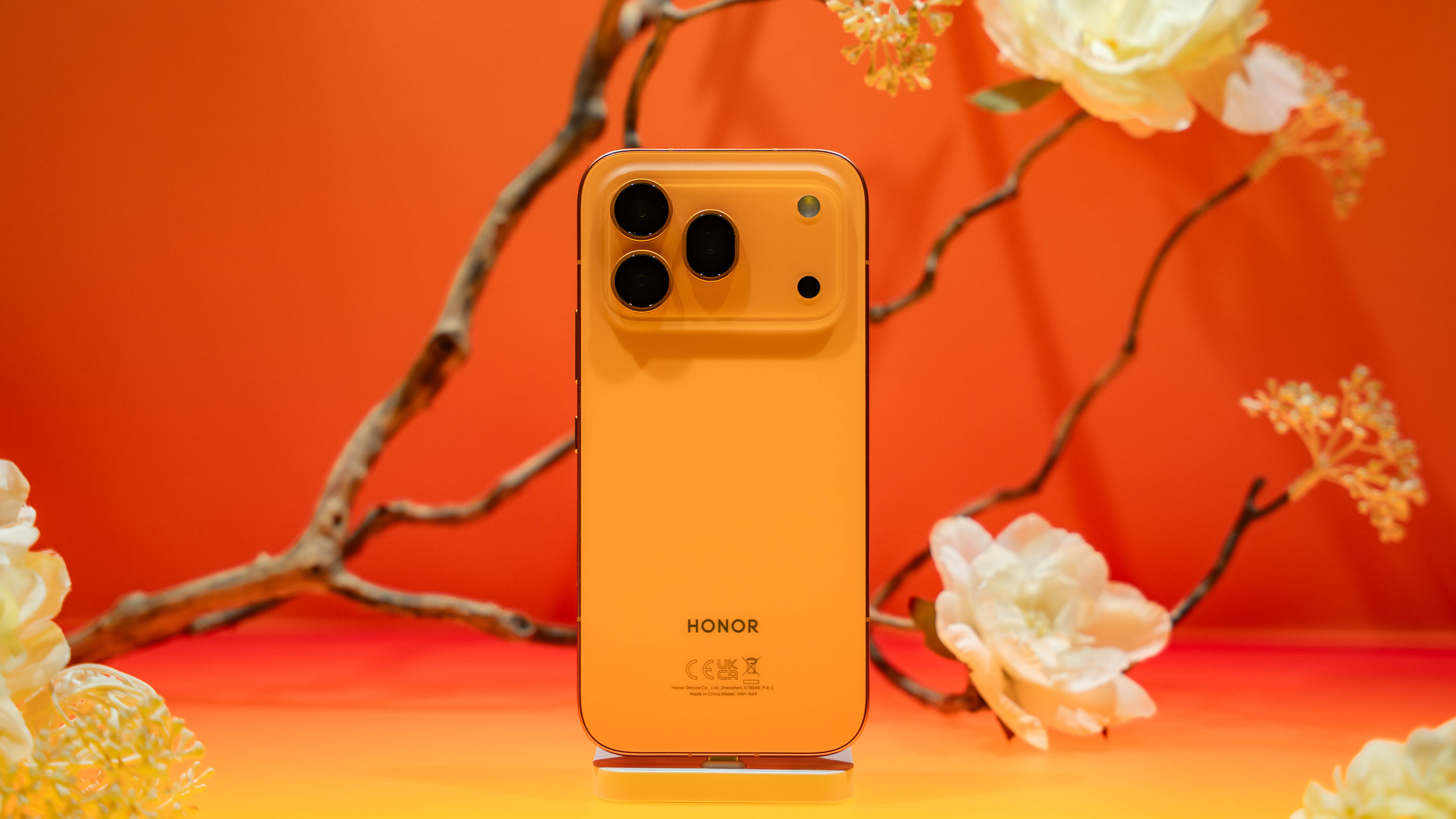 The orange Honor 600 Pro resting on a table in front of some flowers