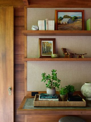 An image of wooden shelves containing photos in frames, plants and a tray.