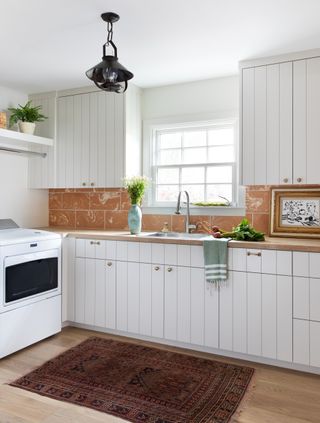 mudroom and laundry room with white cabinets and tile backsplash