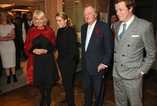 Queen Camilla wearing a red scarf and black dress standing next to her daughter Laura Lopes, ex husband Andrew Parker Bowles and son Tom Parker Bowles, both wearing suits