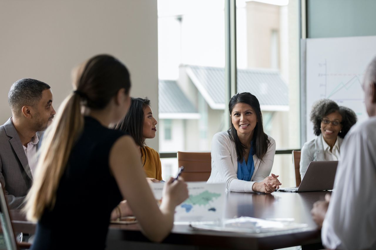 Businesswoman talks with colleagues during weekly meeting.