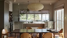 An off white kitchen/ diner with a small island behind the table, and wooden furniture at the table.