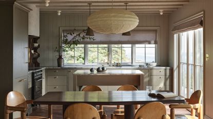 An off white kitchen/ diner with a small island behind the table, and wooden furniture at the table.