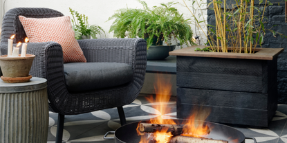 Black rattan chair next to black metal firepit in outdoor living space in garden