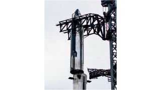 closeup photo of a shiny silver conical spacecraft being placed atop a first-stage booster by the metallic arms of a launch tower.