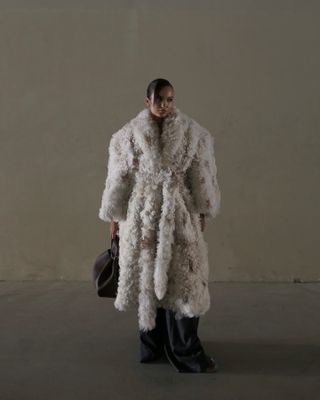 Oumayma Elboumeshouli wearing an oversize shearling wrap coat with a black bag.