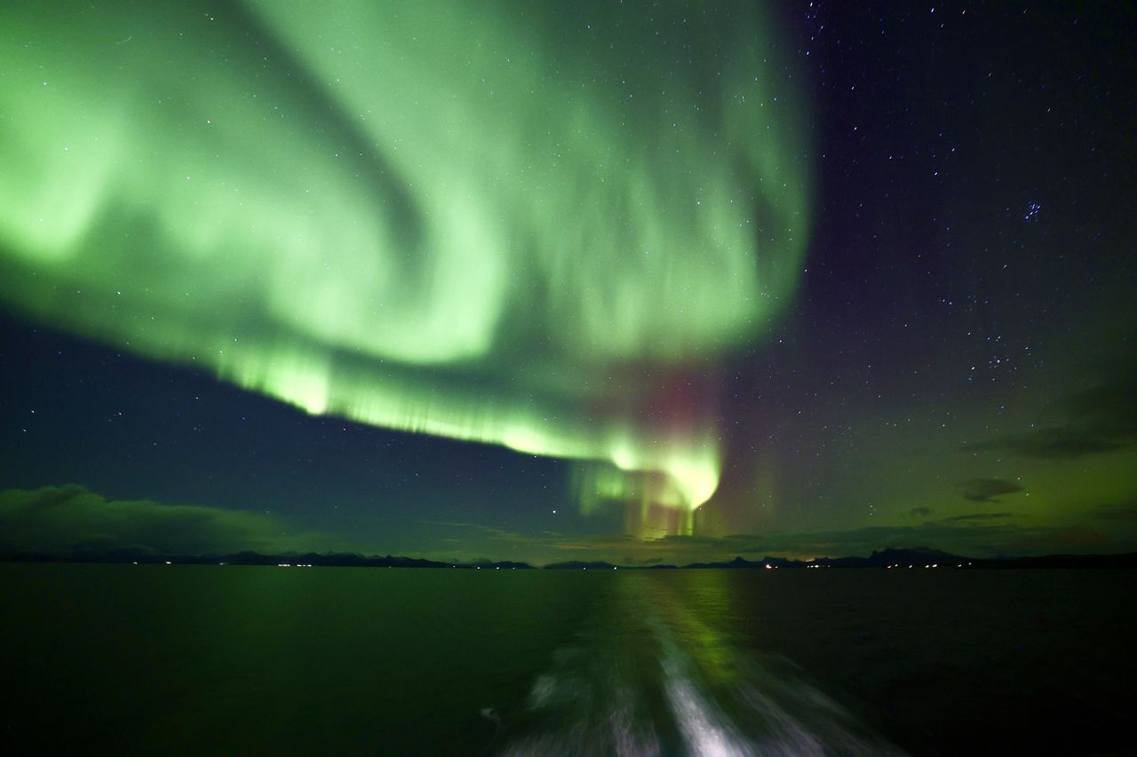 sweeping green northern lights appear as ribbons in the sky reflected in the water below
