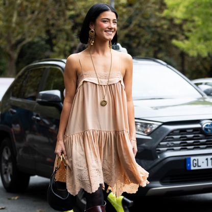 a street style star wearing a summer dress and boots
