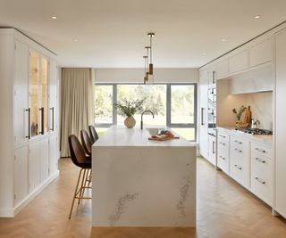 off white galley style kitchen with large central island, wooden floor and large windows at one end of room