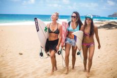 Three women wearing swimwear and carrying surf boards