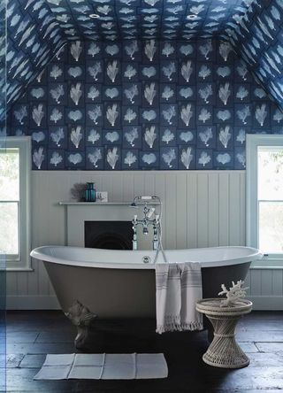 bathroom with grey freestanding rolltop bath with slate flooring and blue patterned wallpaper on walls and ceiling