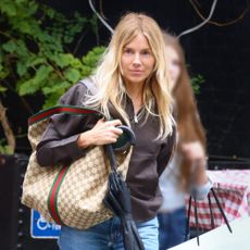 Sienna Miller wears blue jeans, cuffed at the ankle with Miu Miu clogs, a brown jacket and a Gucci bag.
