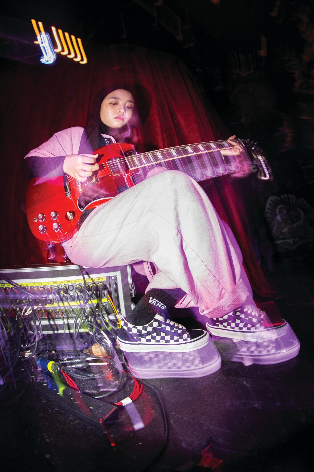 A woman plays guitar and wears Vans sneakers.