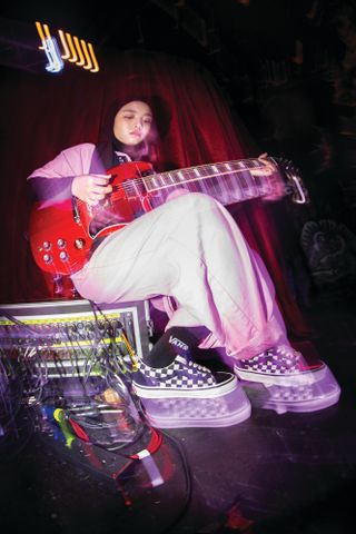 A woman plays guitar and wears Vans sneakers.