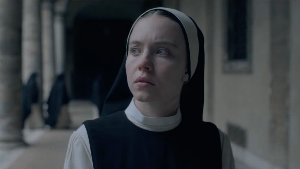 a woman (sydney sweeney) in a nun's habit walks through a hall
