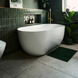 green bathroom with large format grey floor tiles and white freestanding bath with brass taps