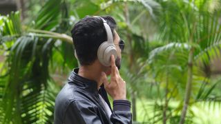 A man wearing the Sony WH-1000XM4 headphones with his hand to the right cup in amongst palm trees