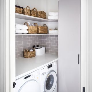 White utility room with washing machine and baskets on shelves.