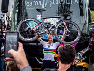 Lotte Kopecky holds her bike aloft for fans in front of her bus