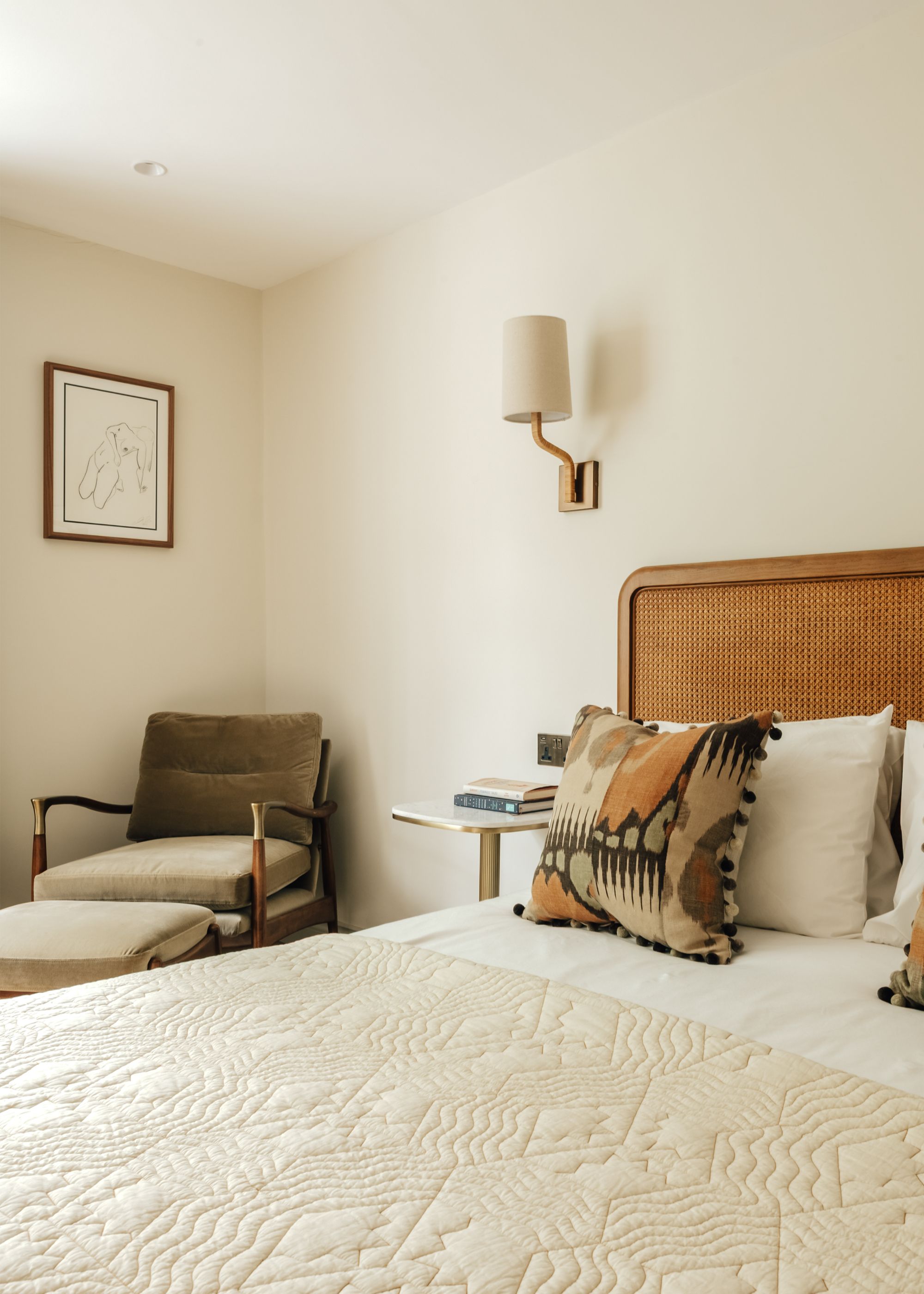 A bedroom with warm white walls, cream bedding, and a rattan headboard.