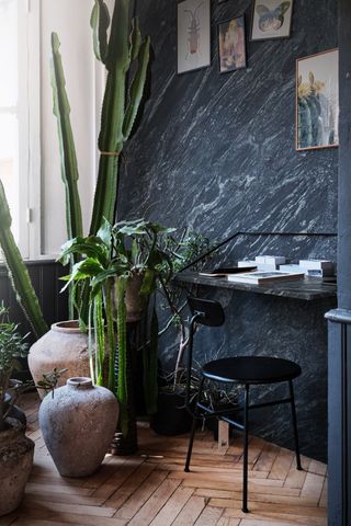 bedroom home office with marble wall and desk, black chair, pots and plants, cactus, artwork on wall, herringbone floor