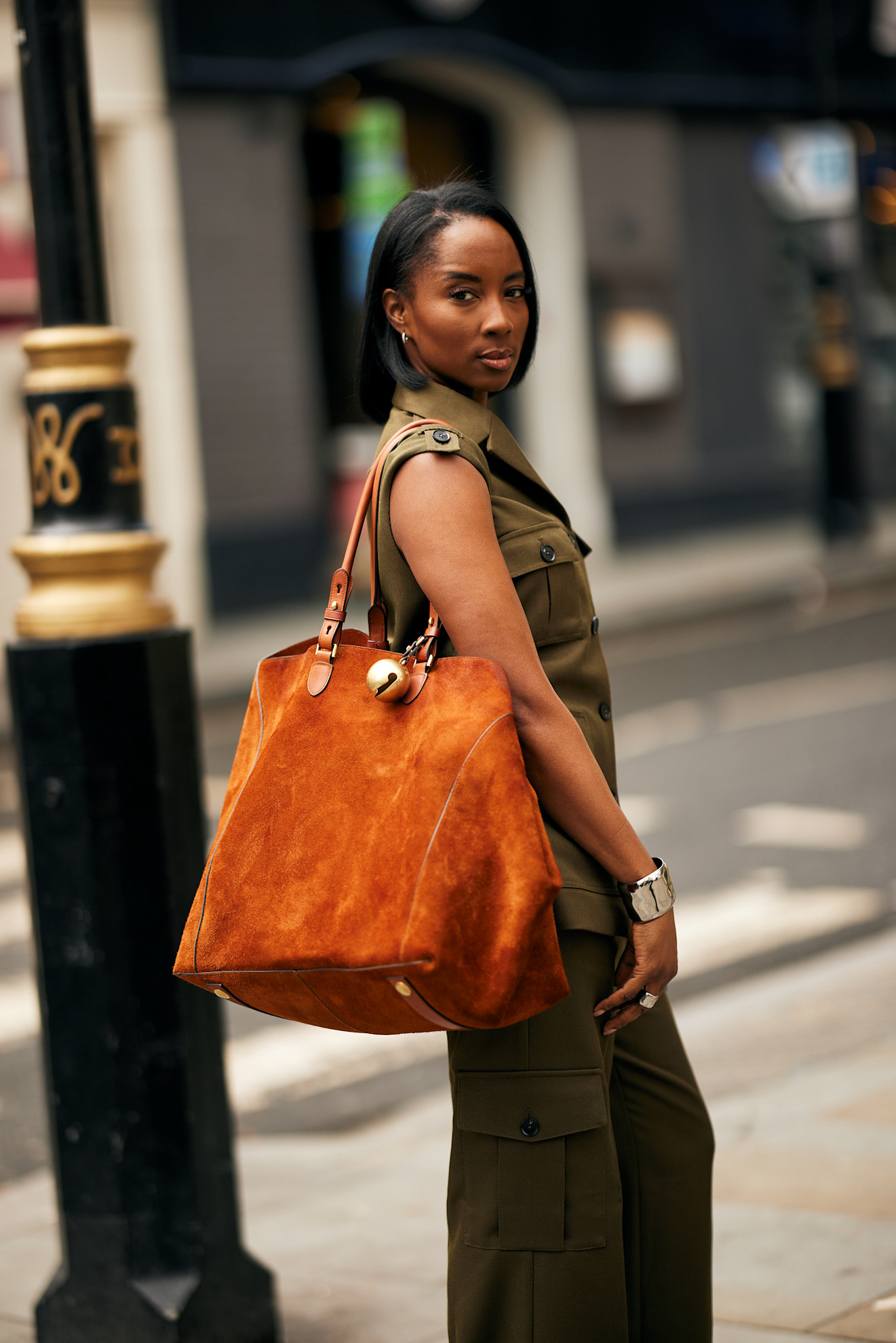 A woman wearing a orange brown suede tote bag and green jumpsuit