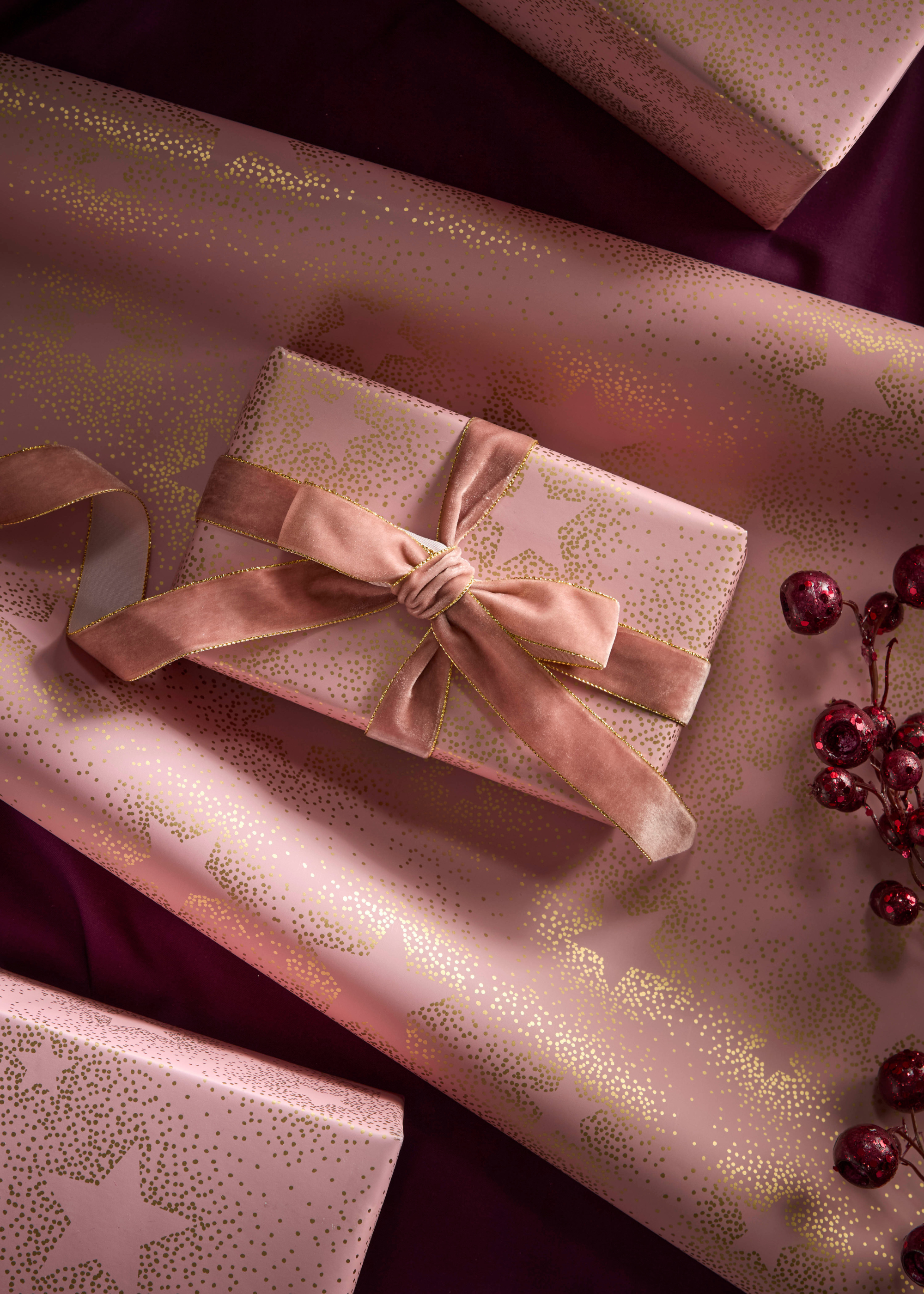 A pale pink wrapping paper with gold dotted star designs and a velvet ribbon to match