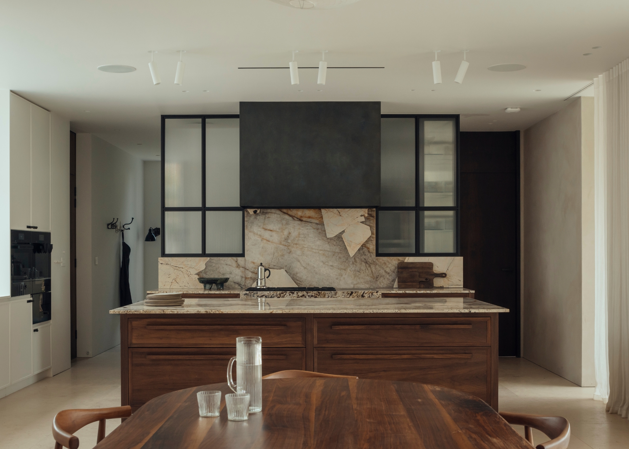 A neutral wooden and beige kitchen with a statement stone countertop and splashback, framed with symmetry