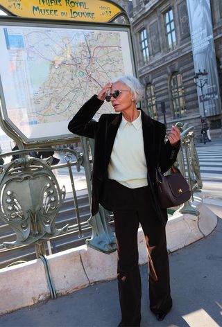 how to wear velvet is shown in a photo of a woman standing on the sidewalk in Paris wearing a dark brown velvet suit with a pistachio button-down shirt layered under a matching sweater with pointed boots and a crescent bag