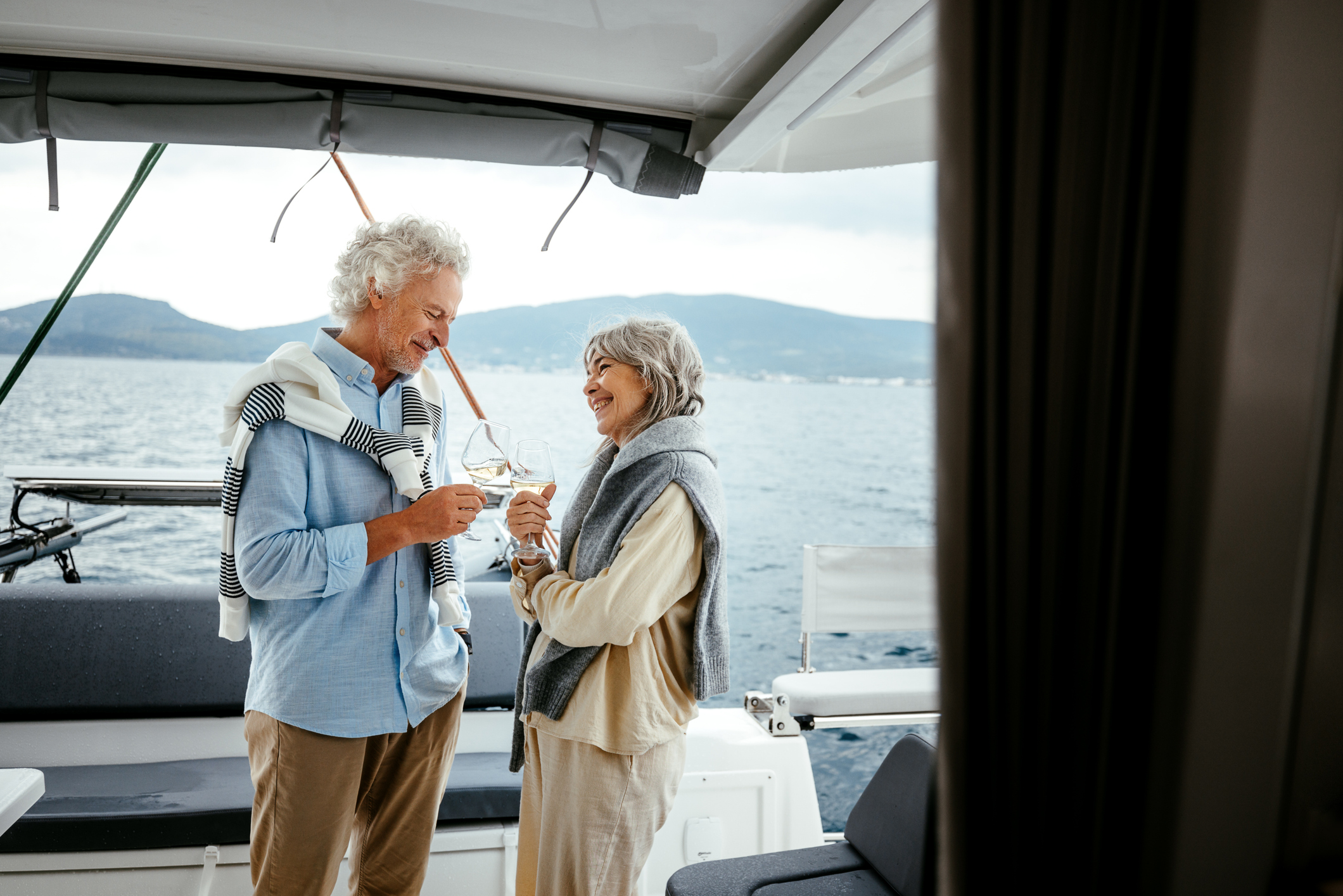 A senior couple relaxing and sharing glasses of wine on a yacht deck. The scene captures warmth, companionship, and a peaceful moment surrounded by the sea.