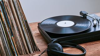 Budget turntable playing a vinyl record with a stack of albums placed next to it