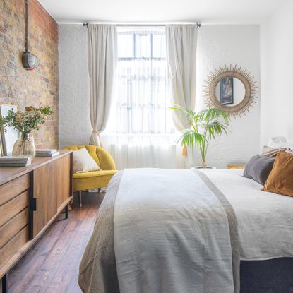 White bedroom with exposed brick wall, sheer curtains and rattan mirror