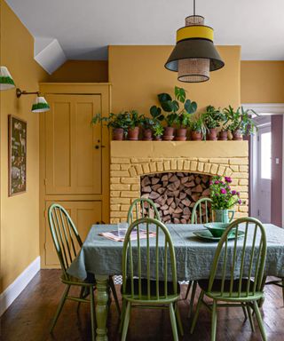 Kitchen eating area with a fireplace and ochre gold coloured painted walls, houseplants, retro pendant light and table and chairs.