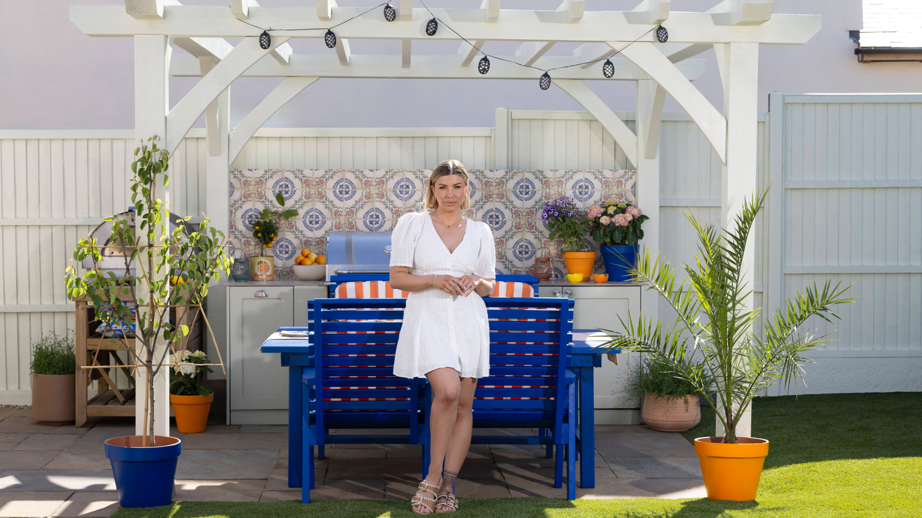 Olivia Bowen in white sundress in front of her pergola and garden dining table.