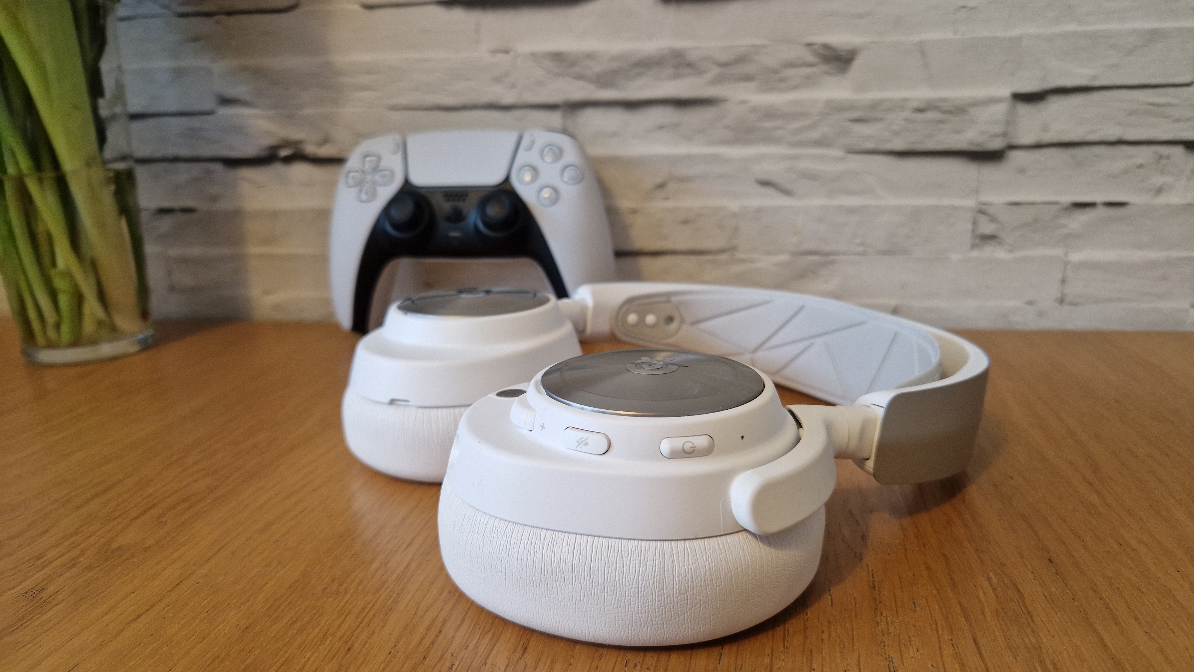 The SteelSeries Arctis Nova Pro Wireless white edition on a wooden surface with a white brick background