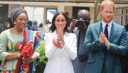 Meghan Markle wearing a white suit in nigeria with a corsage and an aurate necklace