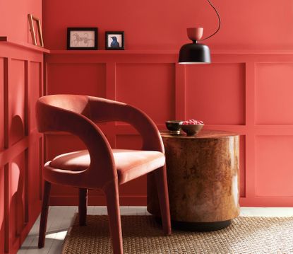 A living room with wood panelling painted a bright and warm red with a modern velvet armchair and cylindrical burlwood table