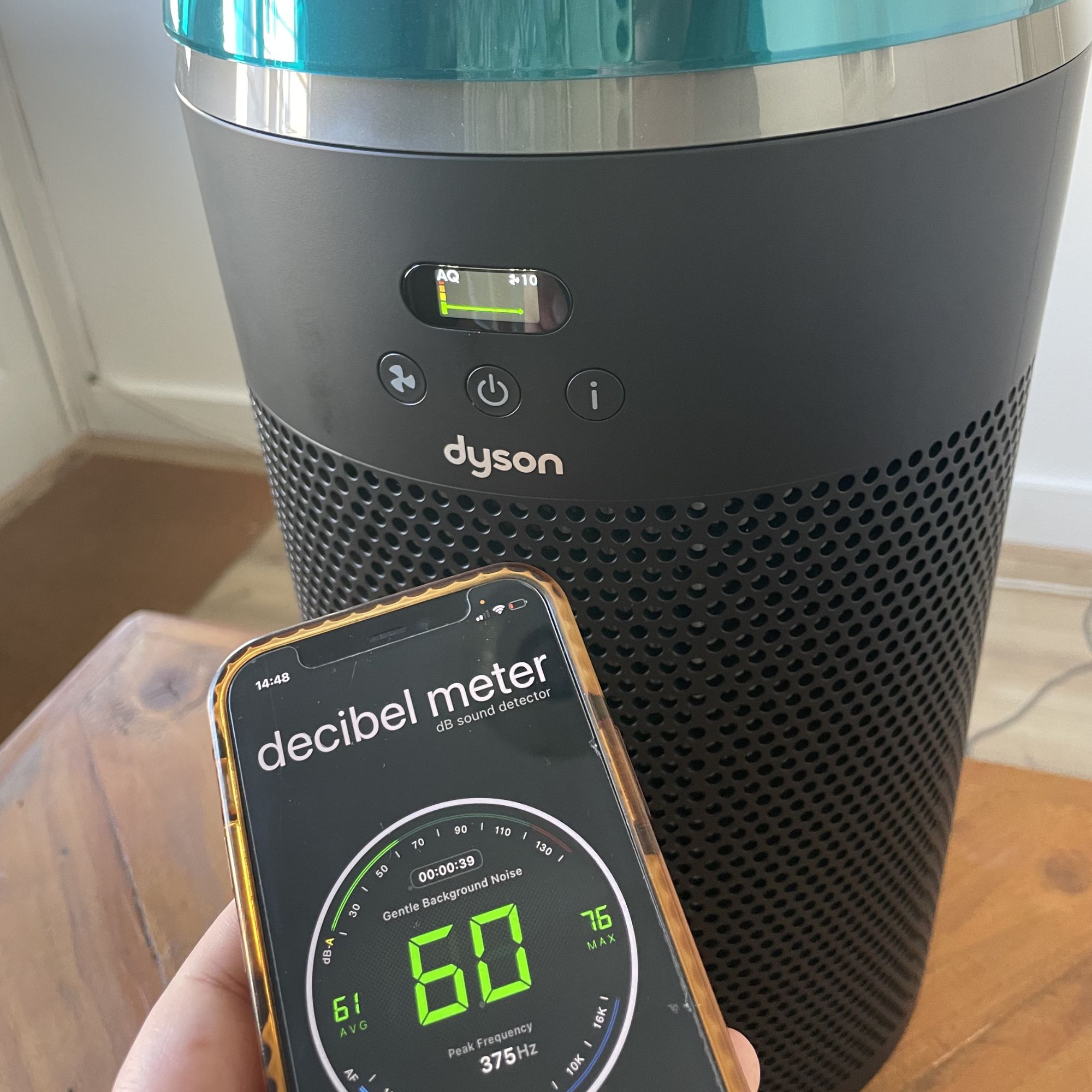 Hand holding a phone with a decibel meter app showing 60dB in front of the Dyson Hushjet Air Purifier