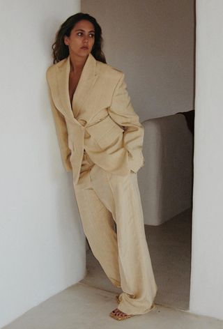 A woman wearing a yellow linen blazer with matching wide-leg trousers and strappy sandals.